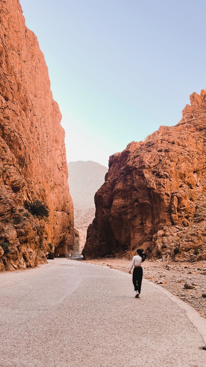 montañas altas en los laterales de una camino asfaltado y chica caminado en el en marruecos